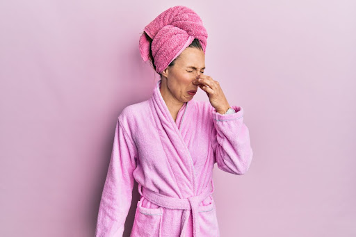 A woman in a bath robe holding her nose due to a bad smell.