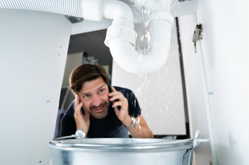Man on the phone with G.F. Bowman plumber as he watches water leak from P-trap underneath sink.